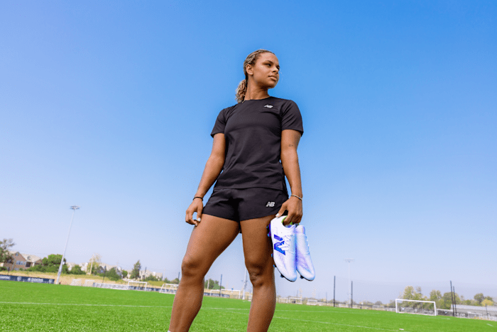 Michelle Cooper holds white and purple New Balance soccer cleats.